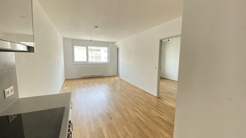 Heller Wohnbereich mit Parkettboden und Zugang zu einem weiteren Zimmer, ideal für offenes Wohnen.