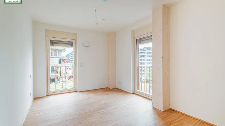 Helles Zimmer mit Holzboden und Zugang zu zwei Balkonen, ideal als Wohn- oder Schlafbereich.