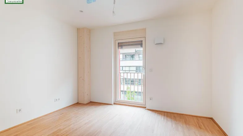 Helles, leeres Zimmer mit Holzboden und Zugang zu einem kleinen Balkon, ideal für individuelle Gestaltung.