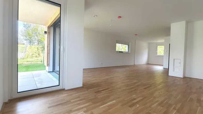 Geräumiger, leerer Wohnbereich mit Parkettboden und großen Fenstern zum Garten.