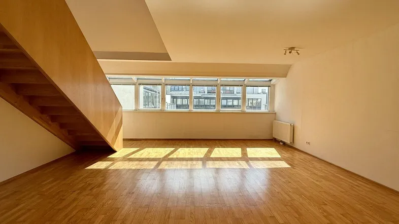 Helles Wohnzimmer mit Holzparkettboden, großen Fenstern und einer Holztreppe, die in eine obere Etage führt.