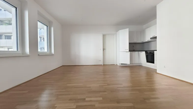 Lichtdurchfluteter Wohnbereich mit großen Fenstern, Parkettboden und integrierter Küchenzeile.