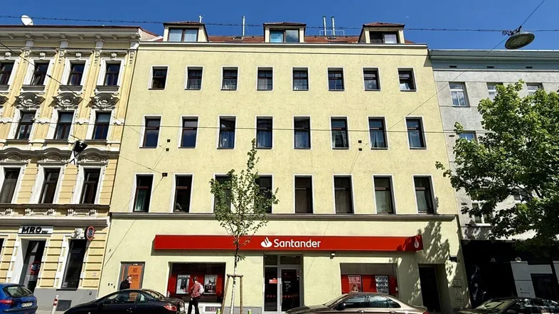 Mehrstöckiges Gebäude mit gelber Fassade und Geschäftsräumen im Erdgeschoss an einer belebten Straße.