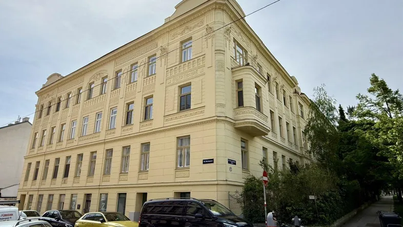 Das historische Gebäude präsentiert sich mit einer hellen Fassade und klassischen architektonischen Details an einer belebten Straße.