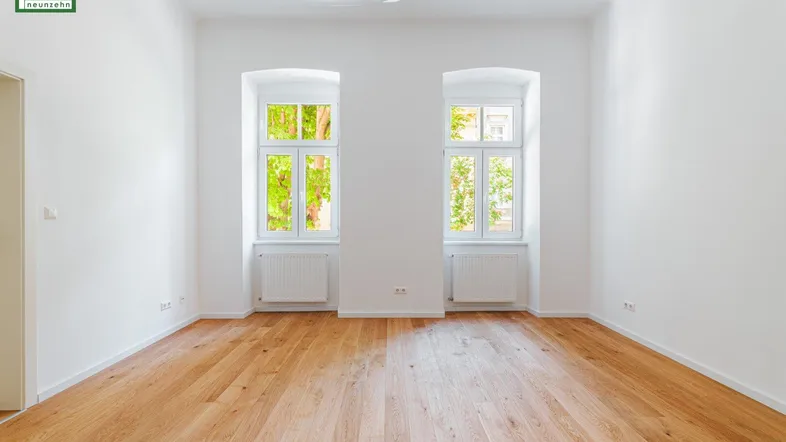 Helles, leeres Zimmer mit neuem Holzparkettboden und zwei großen Fenstern.