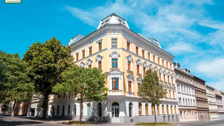 Historisches Eckgebäude mit gelber Fassade und großen Fenstern unter strahlend blauem Himmel.