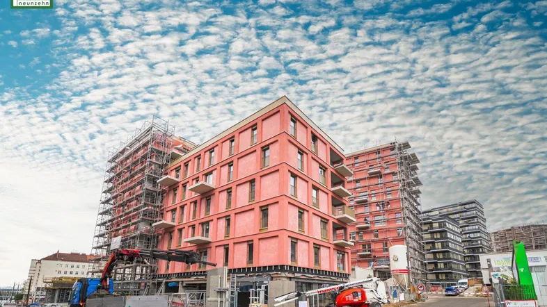 Baustelle mit mehreren im Bau befindlichen Gebäuden und Kränen unter einem bewölkten Himmel.