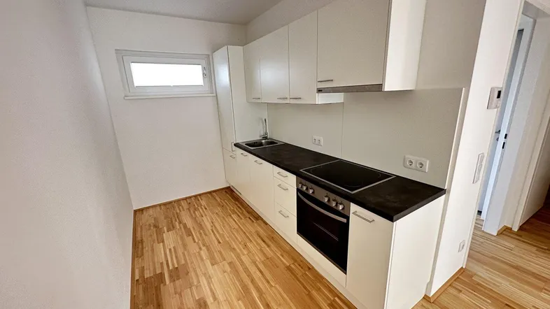 Moderne Einbauküche mit weißen Schränken, dunkler Arbeitsplatte und Holzfußboden in einem hellen Raum.