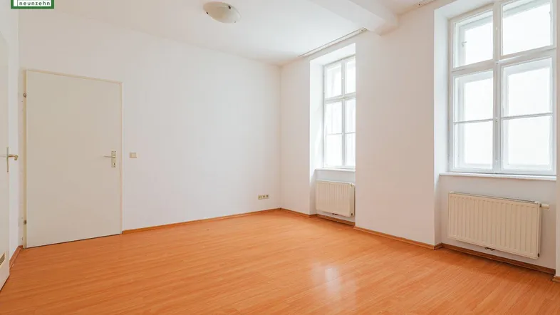 Helles Zimmer mit Laminatboden, weißen Wänden und zwei großen Fenstern, ideal als Wohnraum.