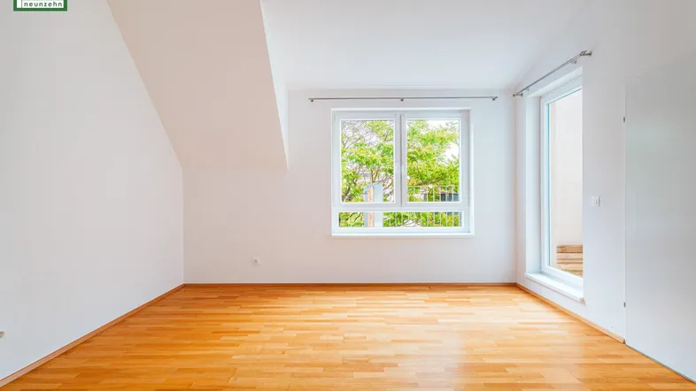 Helles Zimmer mit Holzboden, weißen Wänden und Zugang zu einem Außenbereich.