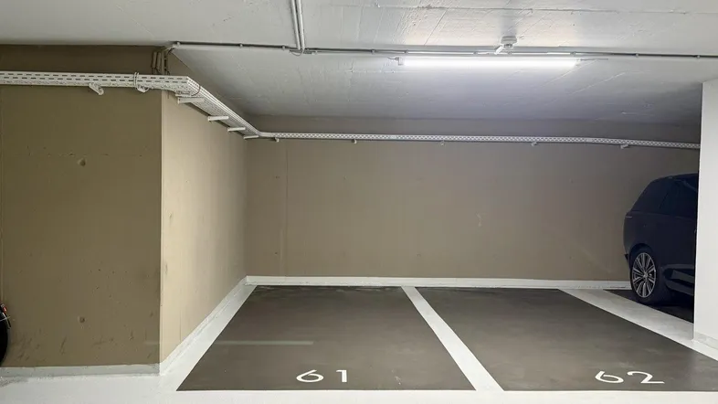 Tiefgarage mit zwei markierten Stellplätzen und sichtbaren Installationen an der Decke.