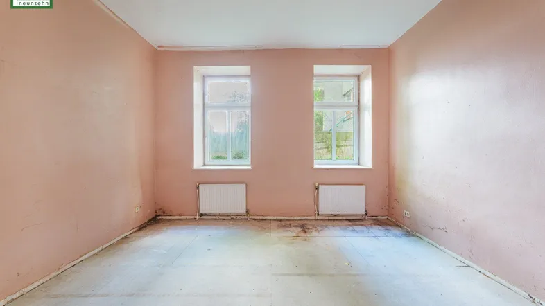 Leerer Raum mit rosa Wänden, zwei Fenstern und Heizkörpern, bereit für eine Renovierung.