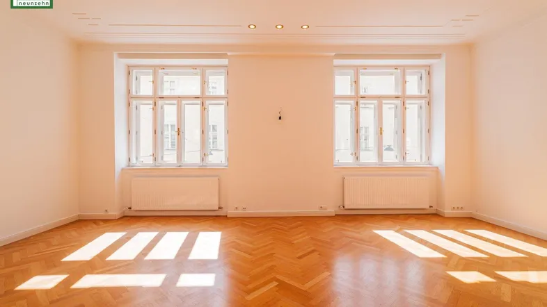 Helles Wohnzimmer mit Fischgrätparkettboden und zwei großen Fenstern, die viel Sonnenlicht hereinlassen.