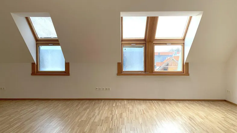 Heller Raum im Dachgeschoss mit schrägen Wänden und zwei großen Dachfenstern, ausgestattet mit Parkettboden.