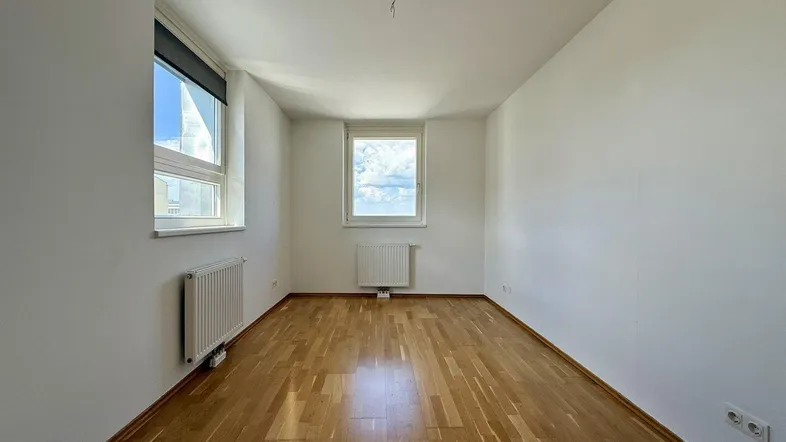 Helles Zimmer mit Parkettboden und zwei Fenstern, ideal als Schlaf- oder Arbeitszimmer.