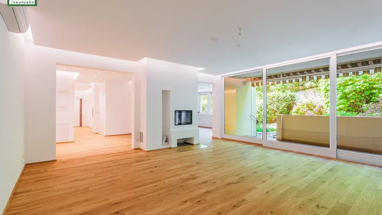 Geräumiges, helles Wohnzimmer mit modernem Kamin, Holzboden und Zugang zu einer grünen Terrasse.