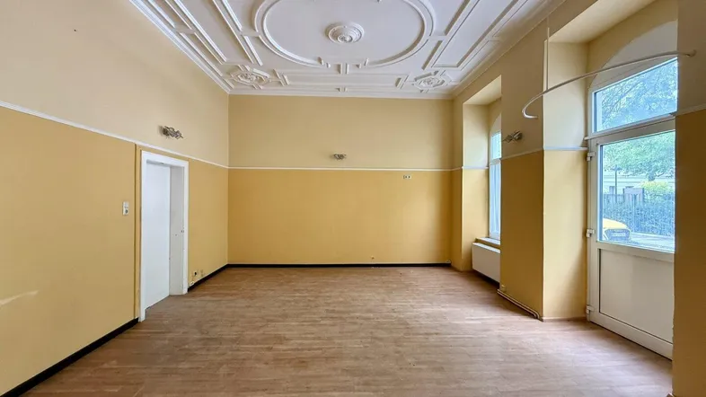 Geräumiger Raum mit hohen Decken, Stuckverzierungen und Holzboden, bereit zur Renovierung und Neugestaltung.