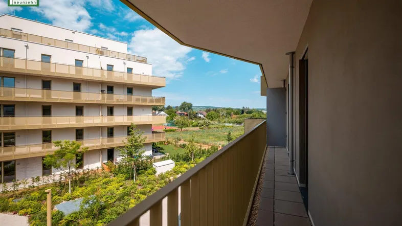 Langer Balkon mit Fliesenboden und Blick auf die umliegenden Gebäude und Grünflächen.
