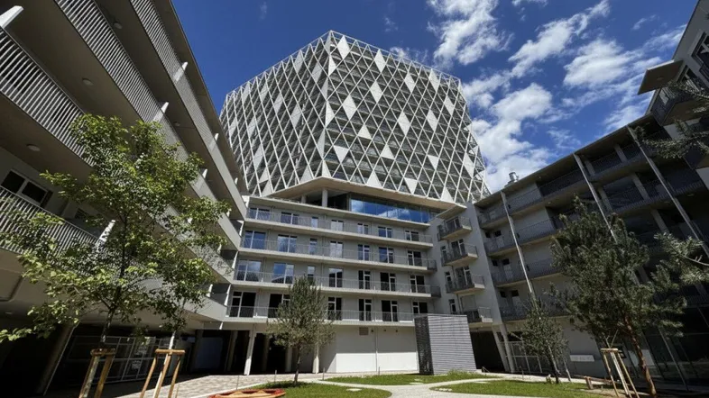Modernes Gebäude mit markanter geometrischer Fassade und begrüntem Innenhof unter blauem Himmel.