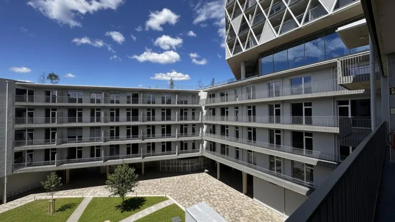Moderne Wohnanlage mit mehreren Gebäuden und einem begrünten Innenhof unter blauem Himmel.