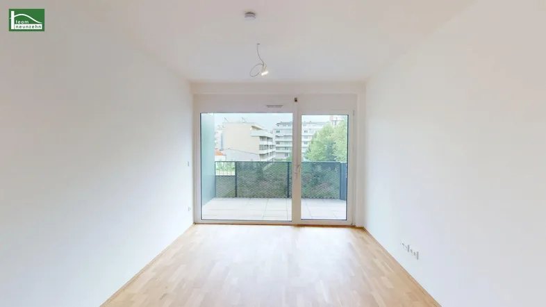 Helles, leeres Zimmer mit Holzboden und Zugang zu einem Balkon mit Stadtblick.
