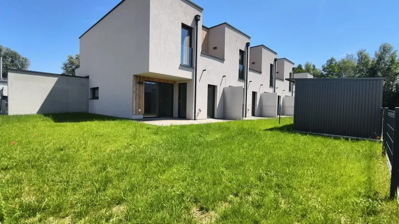 Moderne Reihenhäuser mit heller Fassade, großen Fenstern und einem weitläufigen Rasenbereich unter blauem Himmel.