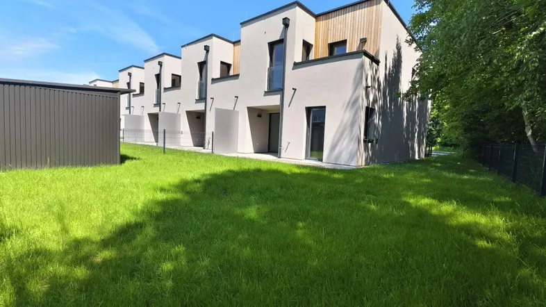 Reihenhäuser mit moderner Architektur, heller Fassade, Holzdetails und gepflegter Rasenfläche unter blauem Himmel.