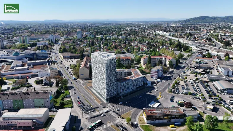 Luftaufnahme eines modernen Gebäudekomplexes in einer städtischen Umgebung mit weitem Blick über die Stadt.
