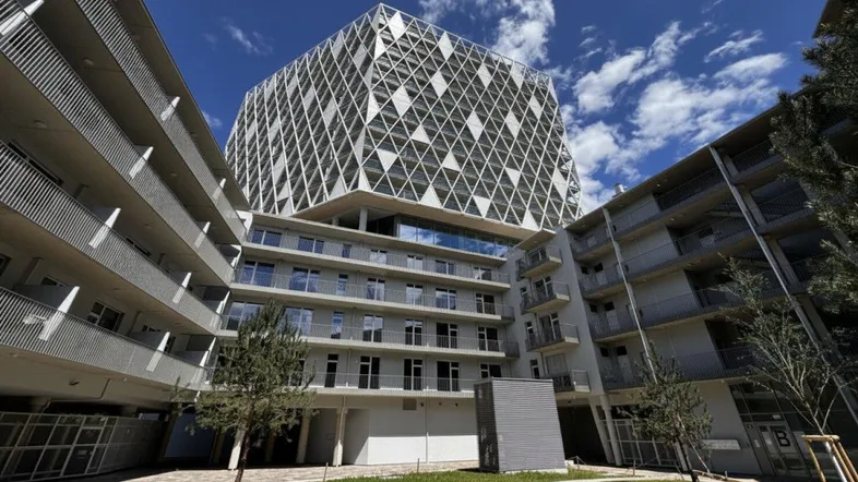 Moderner Gebäudekomplex mit markanter Architektur und begrüntem Innenhof unter blauem Himmel.