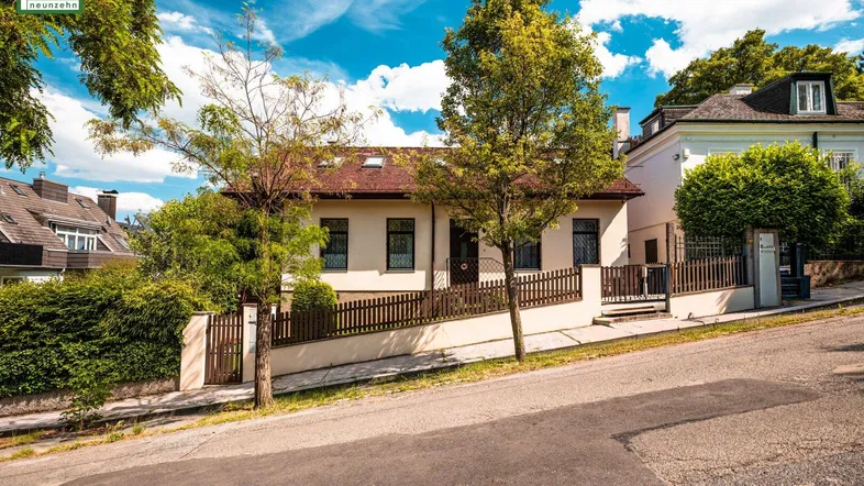 Charmantes Einfamilienhaus mit gepflegtem Vorgarten und Zaun an einer leicht ansteigenden Straße.