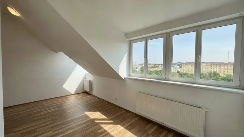 Helles Zimmer im Dachgeschoss mit Laminatboden, großen Fenstern und Blick auf die Stadt.