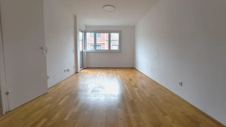 Heller, leerer Raum mit hellem Holzparkettboden und Zugang zu einem Balkon, ideal als Wohnzimmer.