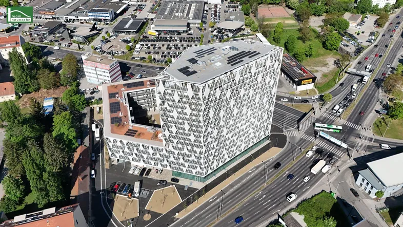Moderne Architektur mit geometrischer Fassade und Solarpaneelen auf dem Dach, umgeben von städtischer Infrastruktur.