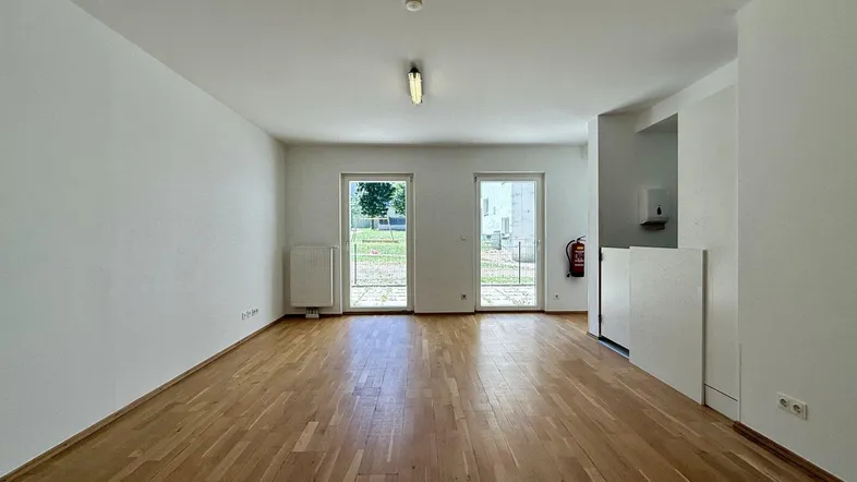 Heller, leerer Raum mit Parkettboden und Zugang zu einem Außenbereich durch Glastüren.