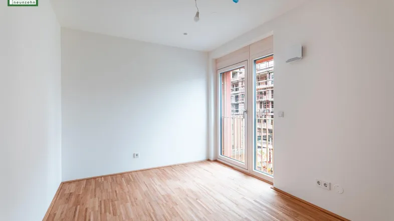 Helles, leeres Zimmer mit Parkettboden und Zugang zu einem französischen Balkon.