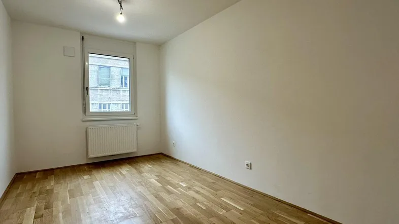 Helles Zimmer mit Parkettboden und weiß gestrichenen Wänden, ideal als Schlaf- oder Arbeitszimmer.