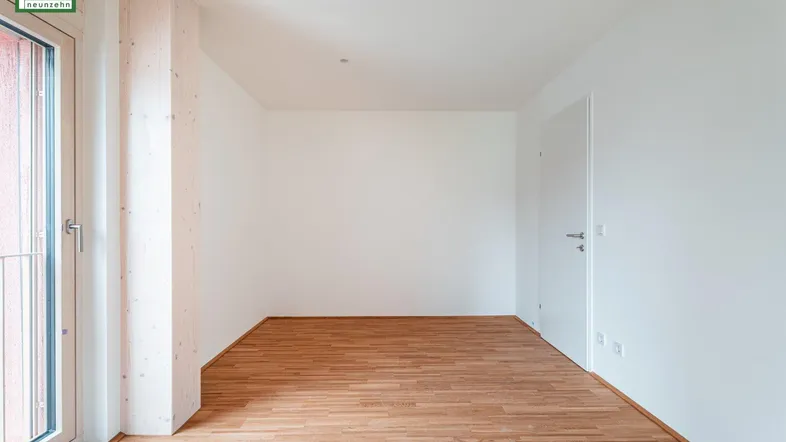 Helles, leeres Zimmer mit Holzboden und Zugang zu einem Balkon, ideal als Wohn- oder Schlafzimmer.