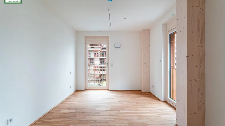 Heller, leerer Raum mit Holzboden, weißen Wänden und Zugang zu einem Balkon.