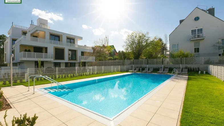Großer Außenpoolbereich mit Liegestühlen und gepflegter Rasenfläche in sonniger Umgebung.