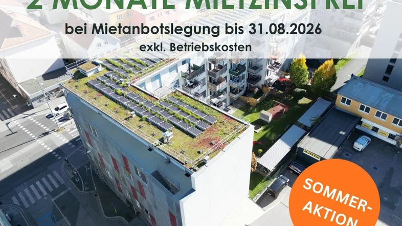 Luftaufnahme eines modernen Gebäudes mit begrüntem Flachdach und Photovoltaikanlage in städtischer Umgebung.
