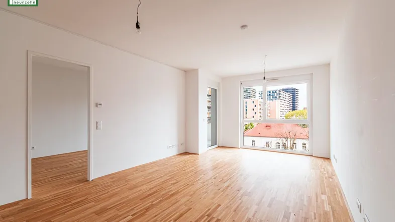 Helles, leeres Zimmer mit Parkettboden und großen Fenstern, die einen Blick auf die Stadt bieten.