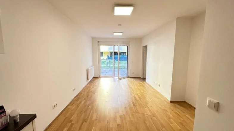 Helles, leeres Wohnzimmer mit Parkettboden und großem Glaszugang zur Terrasse.