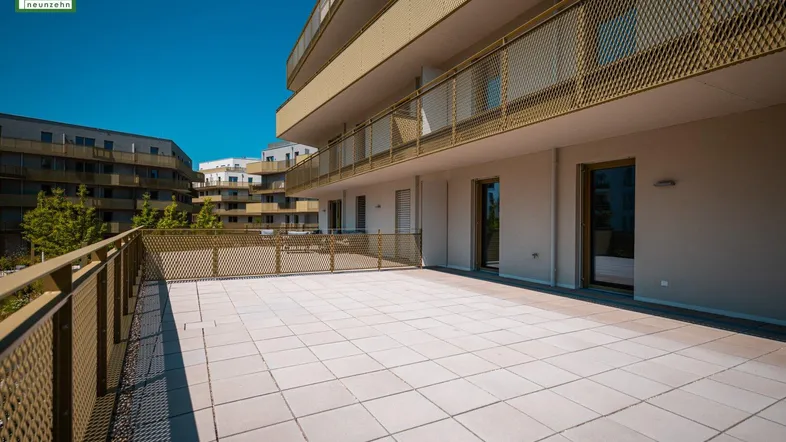 Große, sonnige Terrasse mit Fliesenboden und Blick auf die moderne Wohnanlage.