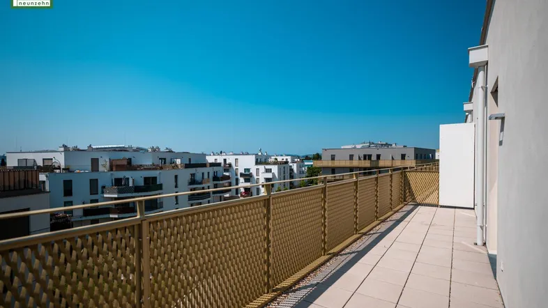 Breiter Balkon mit sonnigem Ausblick auf die umliegenden Neubauten und die Stadtlandschaft.