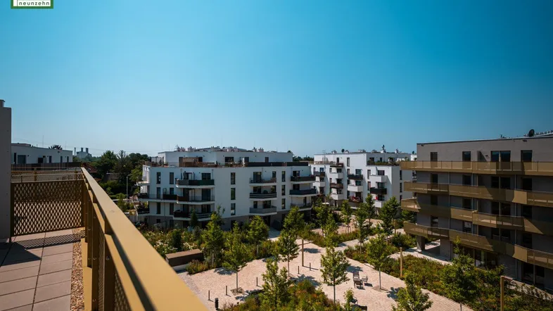 Sonniger Balkon mit Blick auf eine gepflegte Grünanlage und weitere Wohngebäude.
