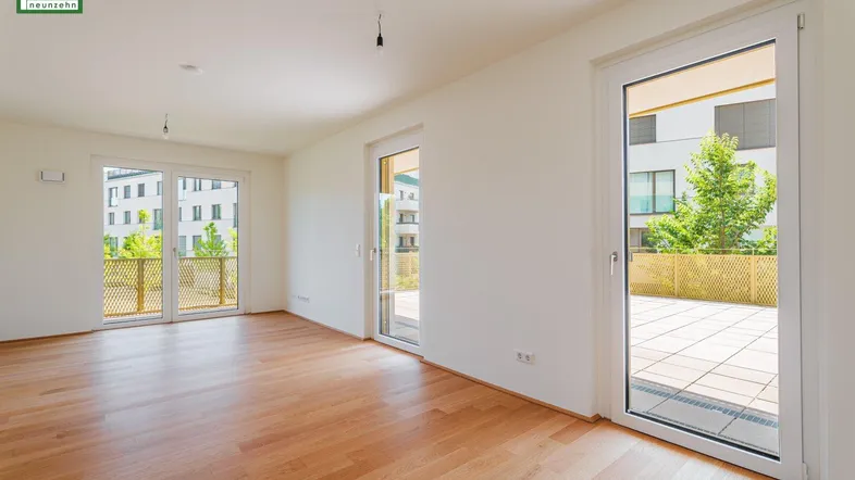 Geräumiges Wohnzimmer mit Holzboden und mehreren Zugängen zu einer großen Terrasse.