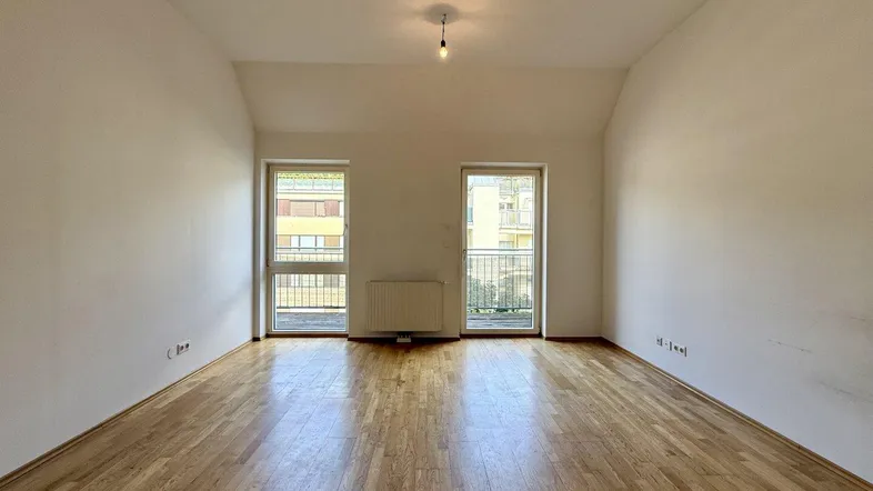 Helles Zimmer mit Holzboden und zwei Fenstertüren, die zu einem französischen Balkon führen.