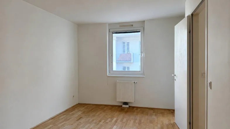 Heller Raum mit Parkettboden, weißen Wänden und einem Fenster, ideal als Wohn- oder Schlafzimmer.
