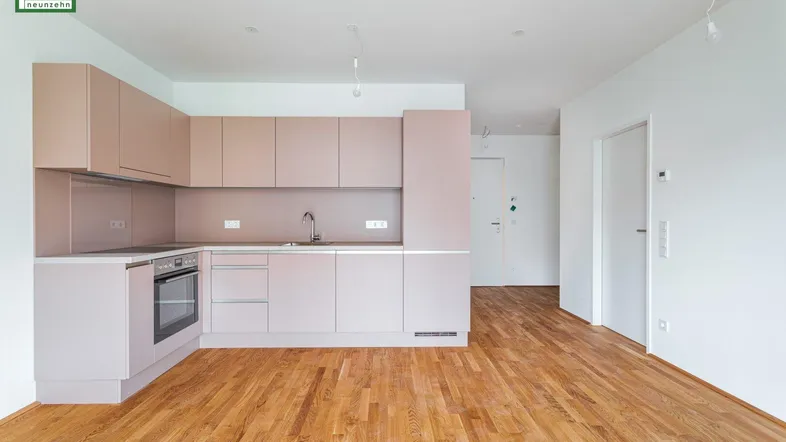 Moderne Einbauküche in hellem Rosaton mit integrierten Geräten und Holzfußboden.