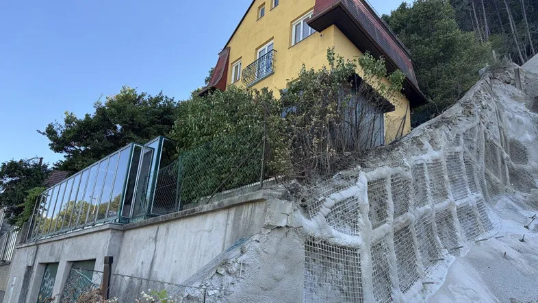 Gelbes Gebäude auf einem Hanggrundstück mit Stützmauer und angrenzender Glasüberdachung.